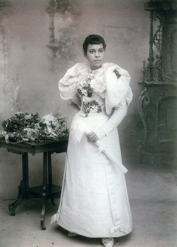 black and white full length portrait of an African American woman in a formal white dress with flowers and holding a scroll in her hand