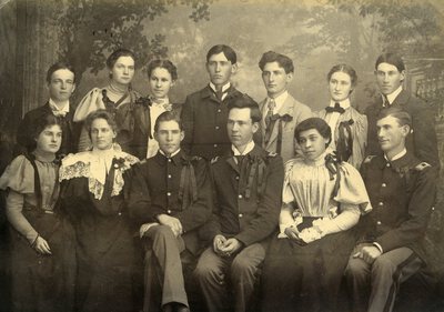 black and white group portrait of 6 women and 7 men in formal clothing with Jennie Eva Hughes seated in the front row