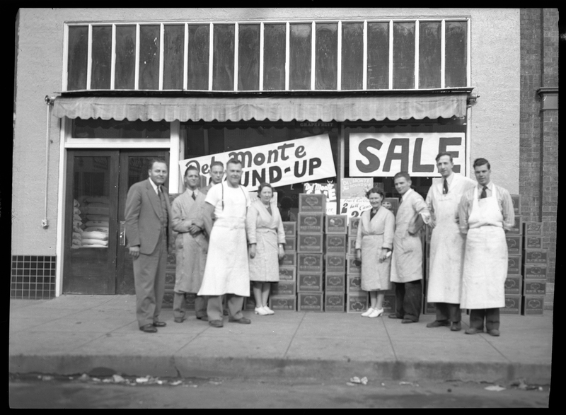 People Standing In Front Of Del Monte Round Up Sign 